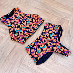 This image features the "Hitchhiker Bottoms- NOW & THEN" by Strange, modeled in a daring and playful spirit. The high-waisted bikini bottoms are showcased in a vibrant cantaloupe color, designed to reverse, as indicated, to a medina pattern.